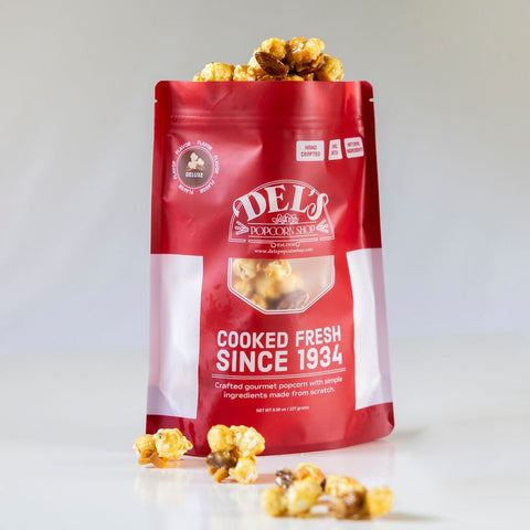 Red bag of Del's Deluxe popcorn with popcorn spilling out on a white background