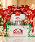 Del's Gourmet Gift Essentials Gift Box  with red bags and white box against a blurred festive background
