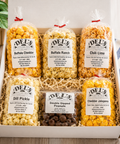 Assorted popcorn flavors in clear bags with visible labels in a box on a wooden surface.