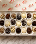 Box of assorted chocolate truffles on a marble surface with Del's logo in the background.