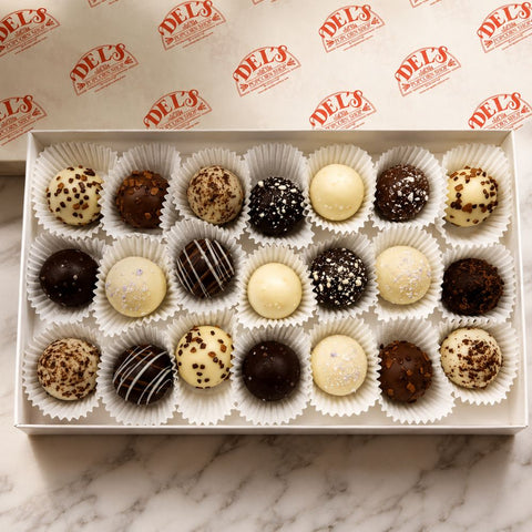Box of assorted chocolate truffles on a marble surface with Del's logo in the background.