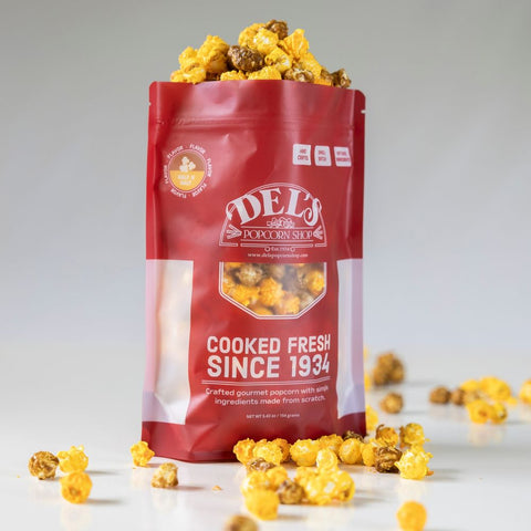 Red bag of Del's half n half Popcorn with popcorn spilling out on a light background