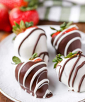 Chocolate-covered strawberries on a white plate with fresh strawberries in the background.