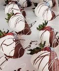 Chocolate-dipped strawberries with white and dark chocolate drizzle on a white surface.