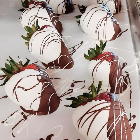 Chocolate-dipped strawberries with white and dark chocolate drizzle on a white surface.