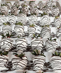 Tray of chocolate-dipped strawberries with white and black drizzle on a white surface.