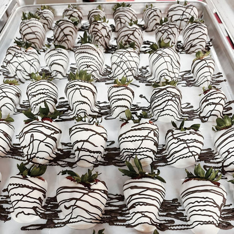 Tray of chocolate-dipped strawberries with white and black drizzle on a white surface.